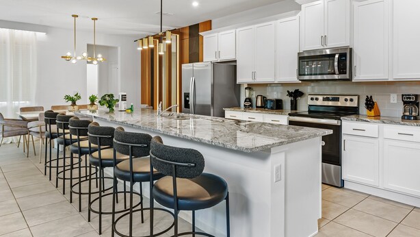 A modern kitchen with white cabinets, a central island with bar stools, stainless steel appliances, and pendant lighting. - Adventure Escape w Epic Themed Bedrooms Private Pool (Kissimmee)
