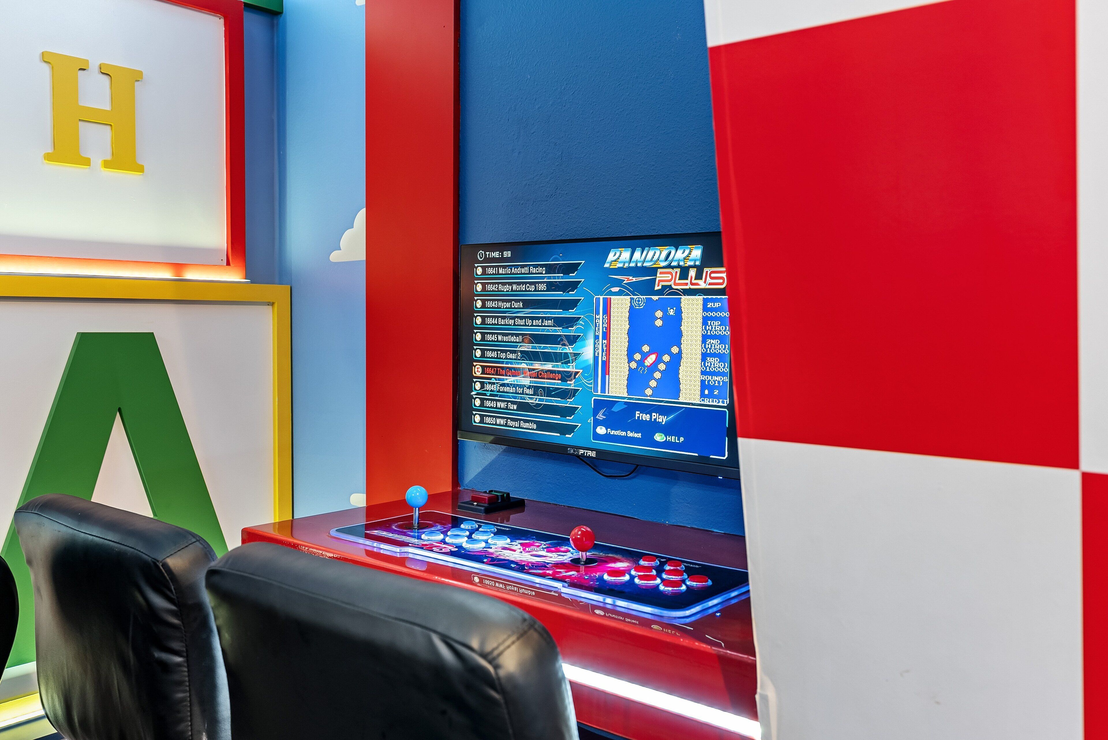 A gaming setup with a monitor displaying a sports game, a joystick, and two chairs.
