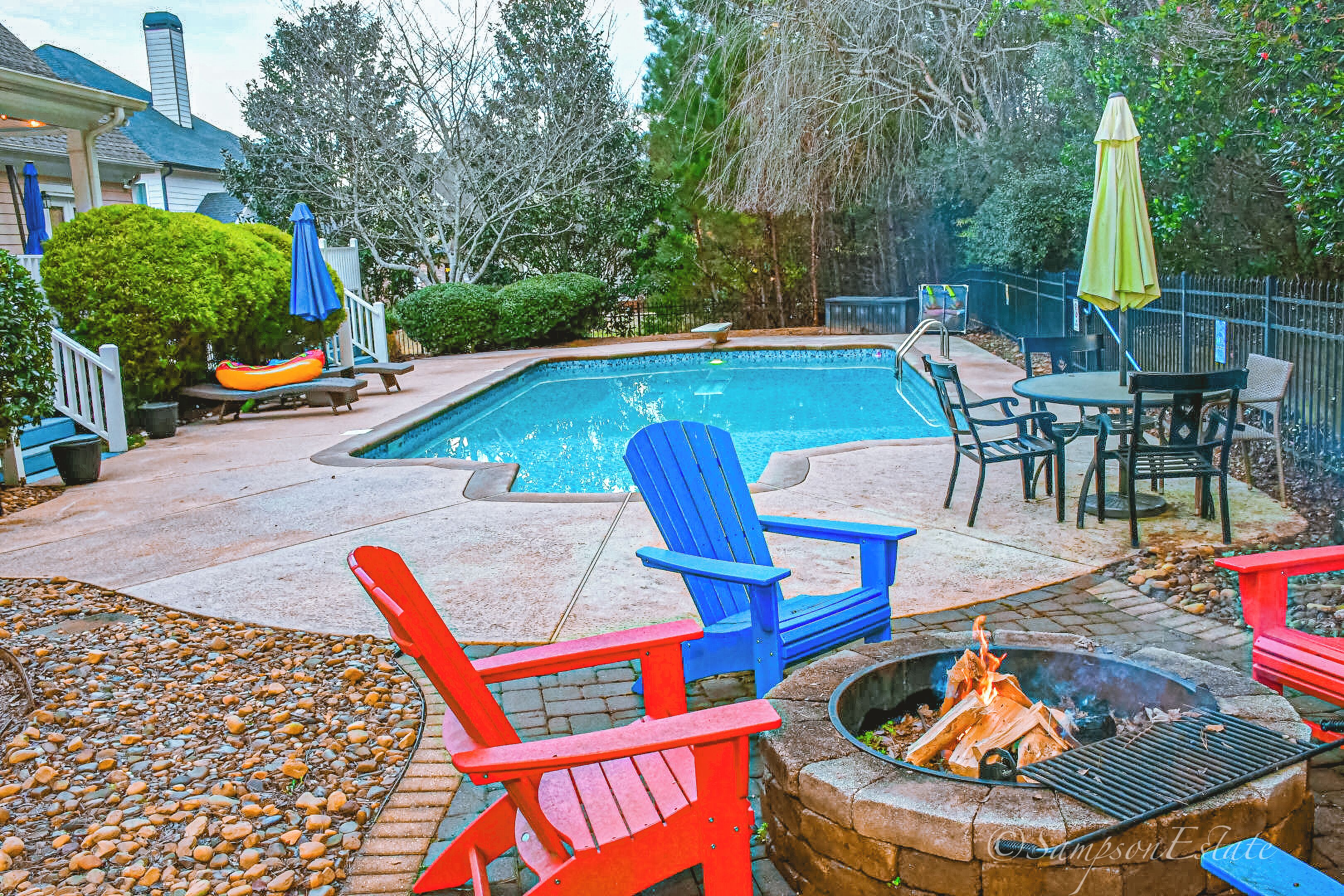 A backyard with a swimming pool, Adirondack chairs, a fire pit, and outdoor furniture.