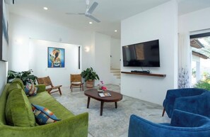 A modern living room with a green sofa, blue armchairs, a coffee table, and a flat-screen TV mounted on the wall. - Private Villa with great ocean views (Sayulita)