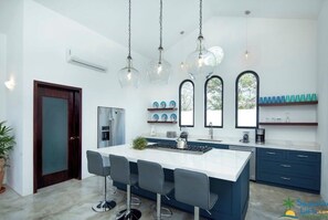 A modern kitchen with a central island, bar stools, pendant lighting, and a view through arched windows. - Private Villa with great ocean views (Sayulita)