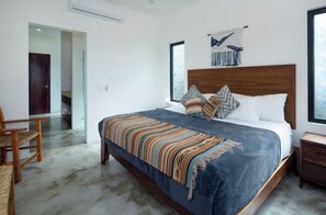 A modern bedroom with a large bed, wooden headboard, and a view of the outdoors through a window. - Private Villa with great ocean views (Sayulita)