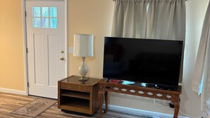 Een woonkamer met een houten vloer, een televisie op een houten dressoir, een lamp en een deur met geëtste glaspanelen.