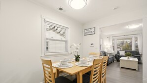 A dining area with a wooden table set for four, surrounded by wooden chairs with black cushions. A vase with white flowers is on the table. - Stylish 3BR, 2BA 8m Away Expo Hub, 12m from Down Town Louisville, 12M from Derby (Louisville)
