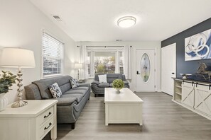 Ein modernes Wohnzimmer mit zwei grauen Sofas, einem weißen Couchtisch und einer weißen Kommode mit einem dekorativen Gegenstand darauf.