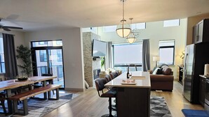 A modern kitchen with a central island, a dining area with a wooden table and benches, and a living area with a sofa and a TV. - Silverthorne Ski Loft - Garage Parking, Hot Tub, Downtown & Minutes to Slopes (Silverthorne)