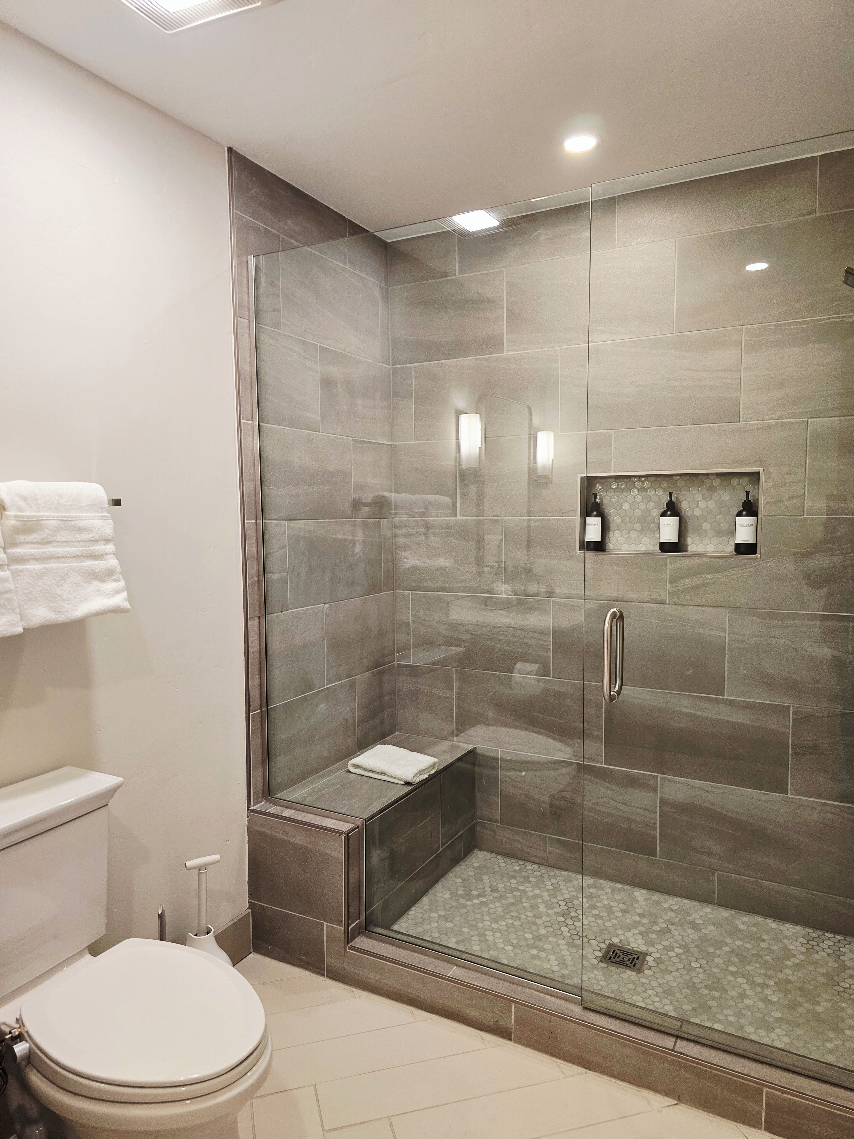 Un baño moderno con ducha de vidrio, inodoro y tocador con perchero.