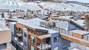 A modern residential area with multi-story buildings, some with balconies, set against a backdrop of snow-covered mountains. - Silverthorne Ski Loft - Garage Parking, Hot Tub, Downtown & Minutes to Slopes (Silverthorne)