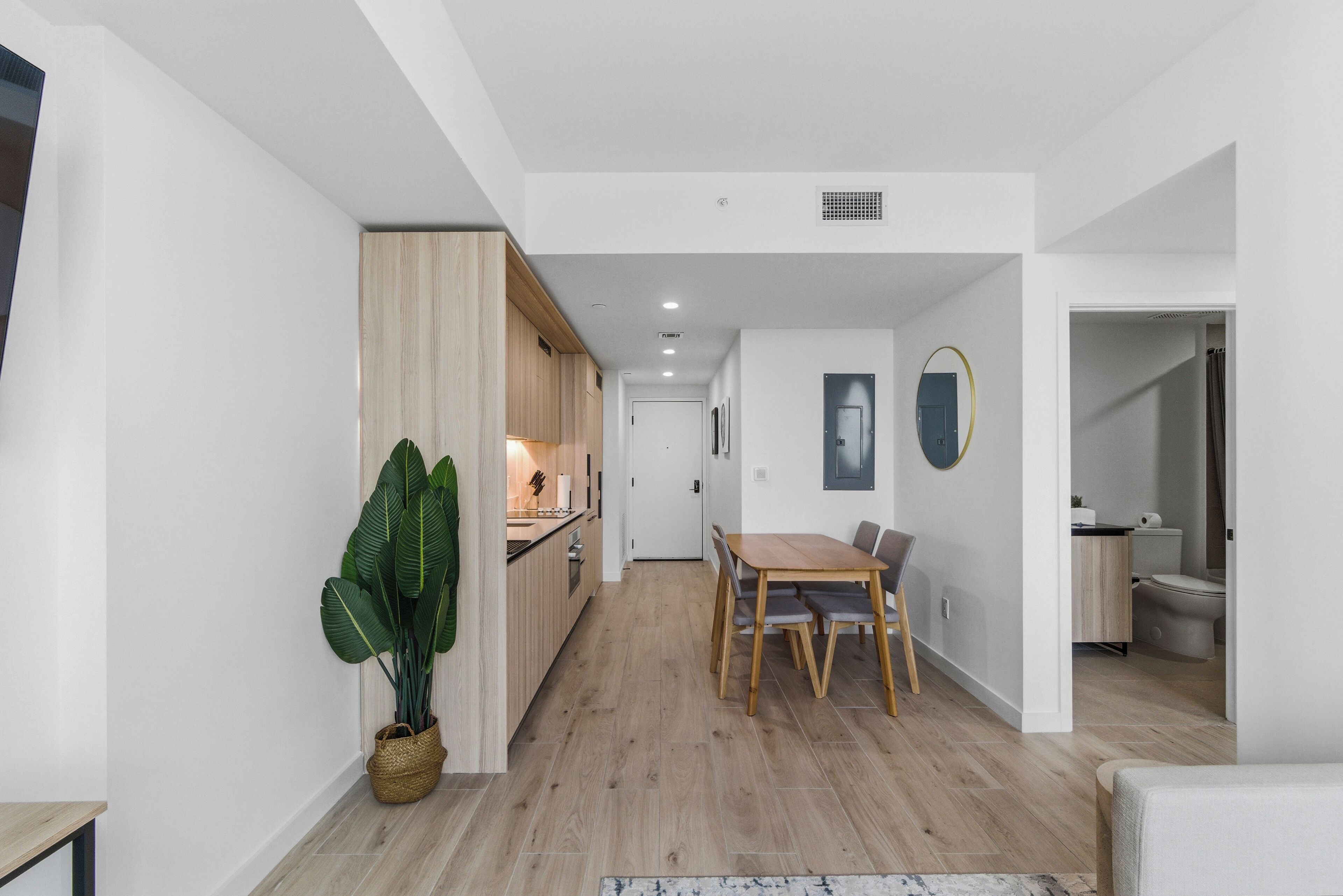 A modern kitchen with wooden cabinets, a dining area with a table and chairs, and a large potted plant.