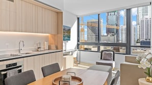 A modern kitchen with a dining area, large windows with a city view, and a view of construction cranes outside. - Downtown Building - Scenic waterfront walking (Miami)