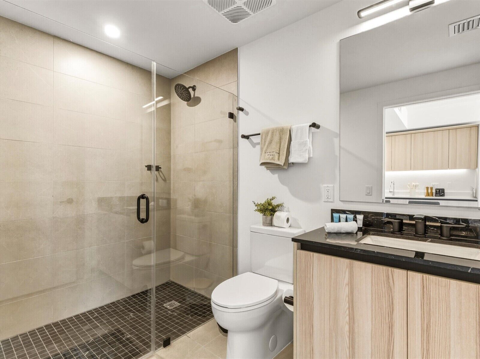 Ein modernes Badezimmer mit einer Glaskabine zur Dusche, einer Toilette, einem Waschbecken mit Spiegel und einem Handtuchhalter.