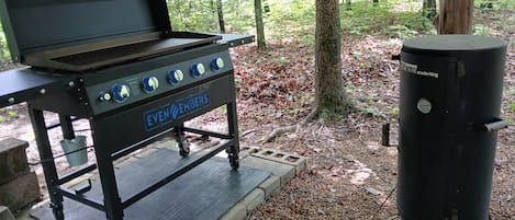 Ein tragbarer Grill mit Rädern, einer Gasflasche und einem Aufkleber mit der Aufschrift 'EVEN EMBERS'.