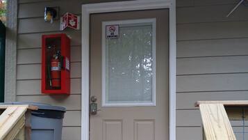 A front door with a 'No Smoking' sign, a fire extinguisher, and a trash bin outside.