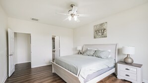 Um quarto com uma cama, mesas de cabeceira, um ventilador de teto e uma porta que dá para um armário.
