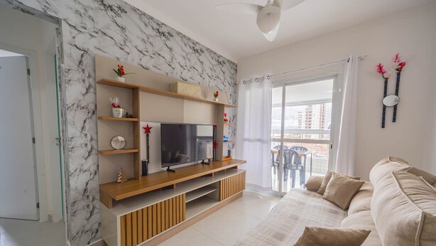 A modern living room with a TV, wooden shelves, and a beige sofa. - Apto com Garagem e Varanda a 450m da Praia (Praia Grande)