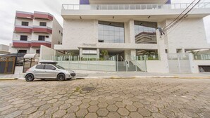 A building with a sign reading "Personnitude" on the ground floor, featuring a staircase leading to the entrance, a car parked in front, and a gated driveway. - Apto com Garagem e Varanda a 450m da Praia (Praia Grande)