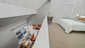 Ein Schlafzimmer mit schr ägen Wänden, einem Bett, einem Schreibtisch mit Stuhl, einem Fenster und einer Tür.