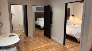 Ein Hotelzimmer mit Holzboden, einem Bett mit weißer Bettwäsche, einem Schreibtisch mit Stuhl und einem an der Wand befestigten Fernseher.