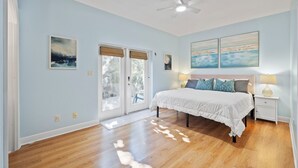 A bedroom with a bed, two bedside tables, a ceiling fan, and a view through the glass doors. - Coastal Villa, Walk to the Beach (Cape Canaveral)