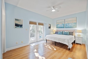 A bedroom with a bed, two bedside tables, a ceiling fan, and a view through the glass doors. - Coastal Villa, Walk to the Beach (Cape Canaveral)