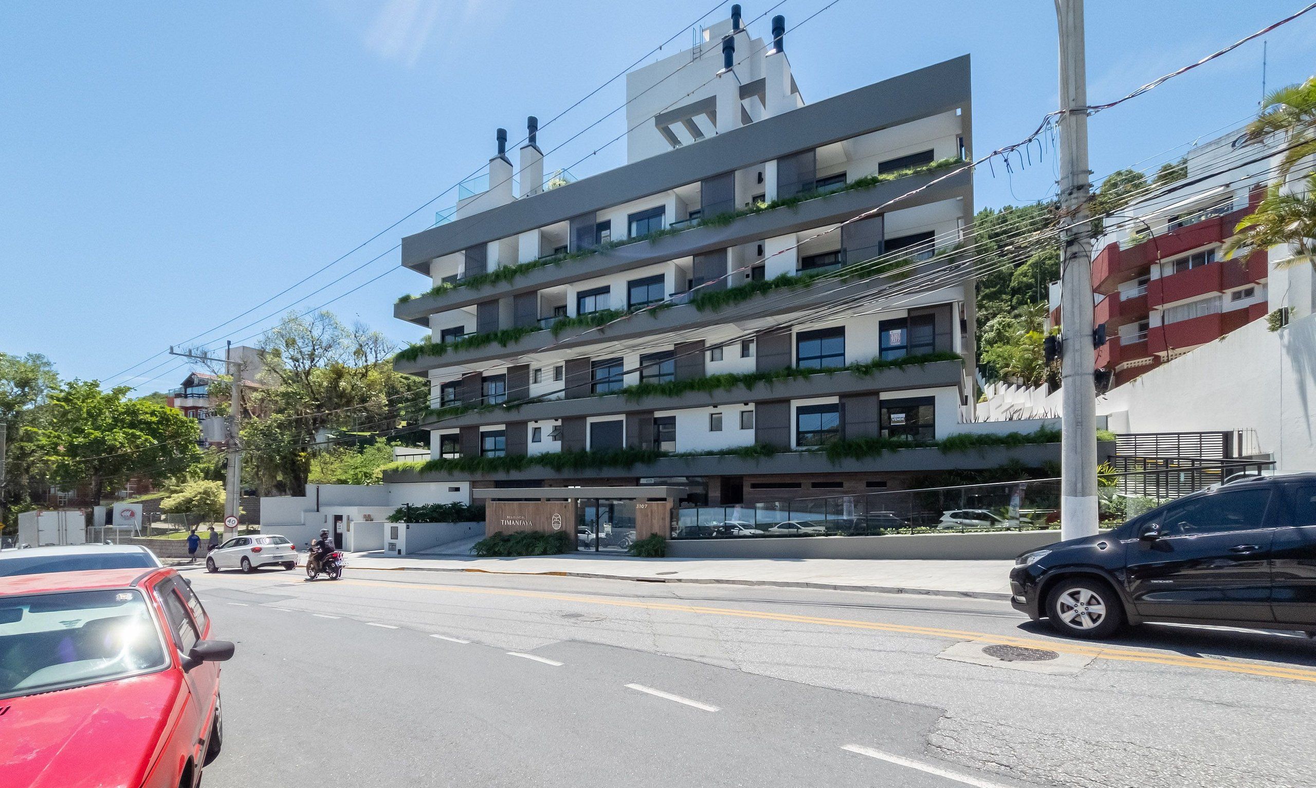 Un edificio de varios pisos con balcones, una entrada visible y coches aparcados.