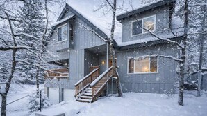 Ett tvåvåningshus med en trätrappa som leder upp till ytterdörren, omgivet av snötäckta träd.
