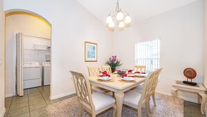 A dining area with a table set for four, chairs, a chandelier, a window, and a laundry room in the background. - Perfect pool & spa villa near Disney World (Davenport)