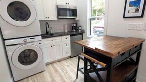 Cozinha compacta com máquina de lavar, micro-ondas e mesa de madeira com gavetas.