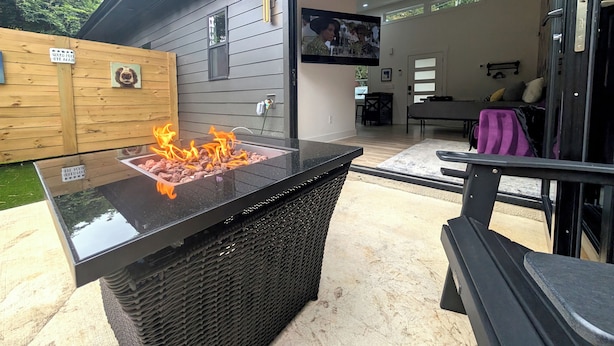 Um pátio externo com uma lareira preta, uma mesa de vime e uma área de estar.