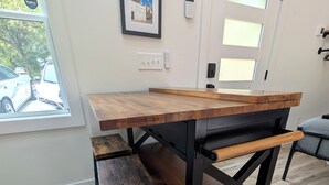 Uma cozinha moderna com uma mesa e banco de madeira, um quadro na parede e vista para carros estacionados lá fora.