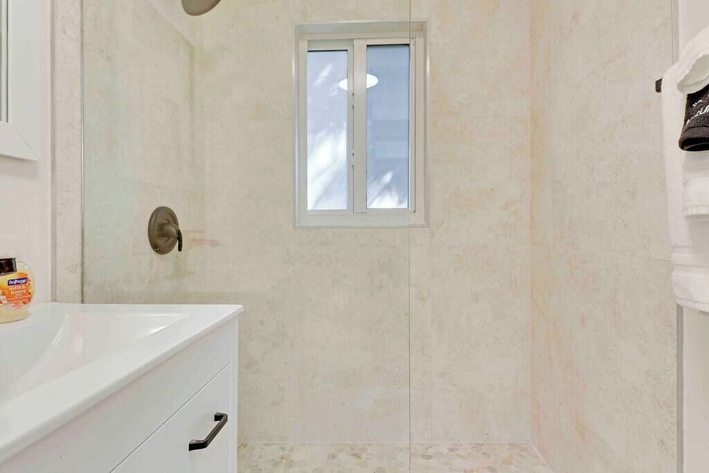 Een badkamer met een douche, een raam en een wit wastafelmeubel.