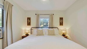 A neatly made bed with white linens and two decorative pillows, flanked by bedside lamps and framed artwork on the walls. - Cottage on California (Stuart)
