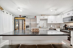 Een moderne keuken met witte kastjes, een groot kookeiland, roestvrijstalen apparatuur en een backsplash met een visgraatmotief.