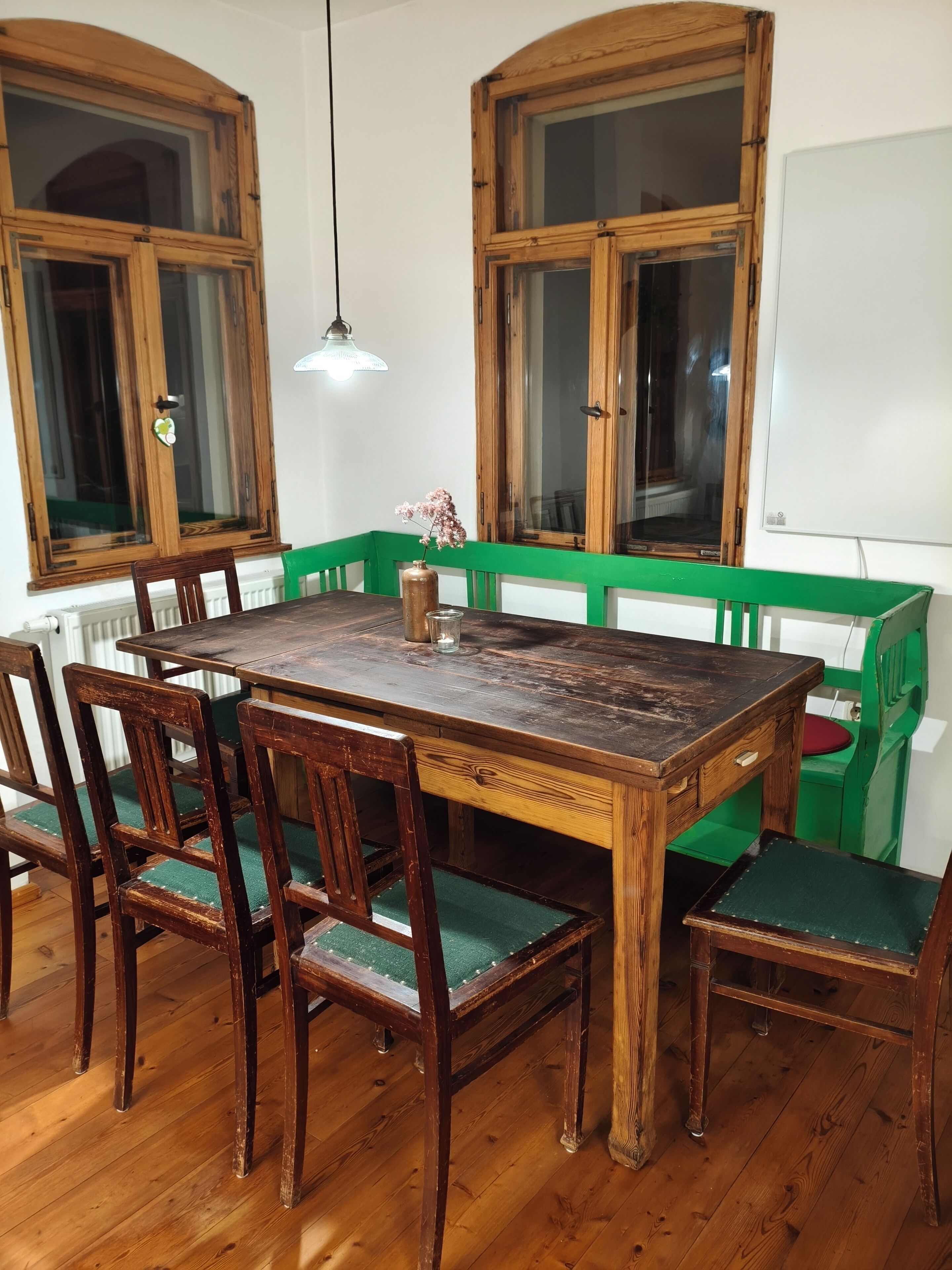 Un comedor con una mesa y sillas de madera, un florero con flores, y bancos acolchados verdes.