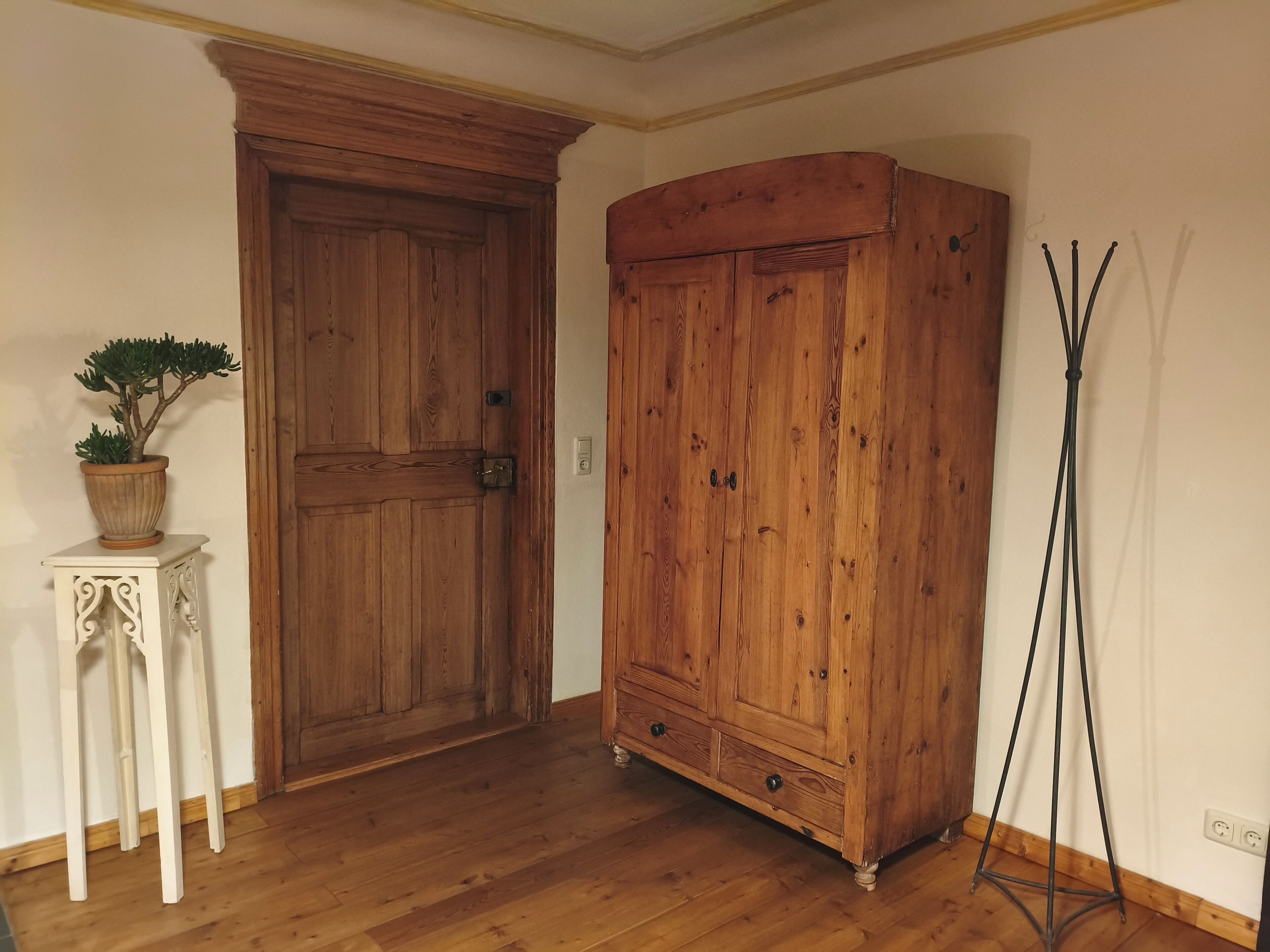 Una stanza con una porta in legno, un armadio, un piccolo tavolo con una pianta e una lampada da terra.