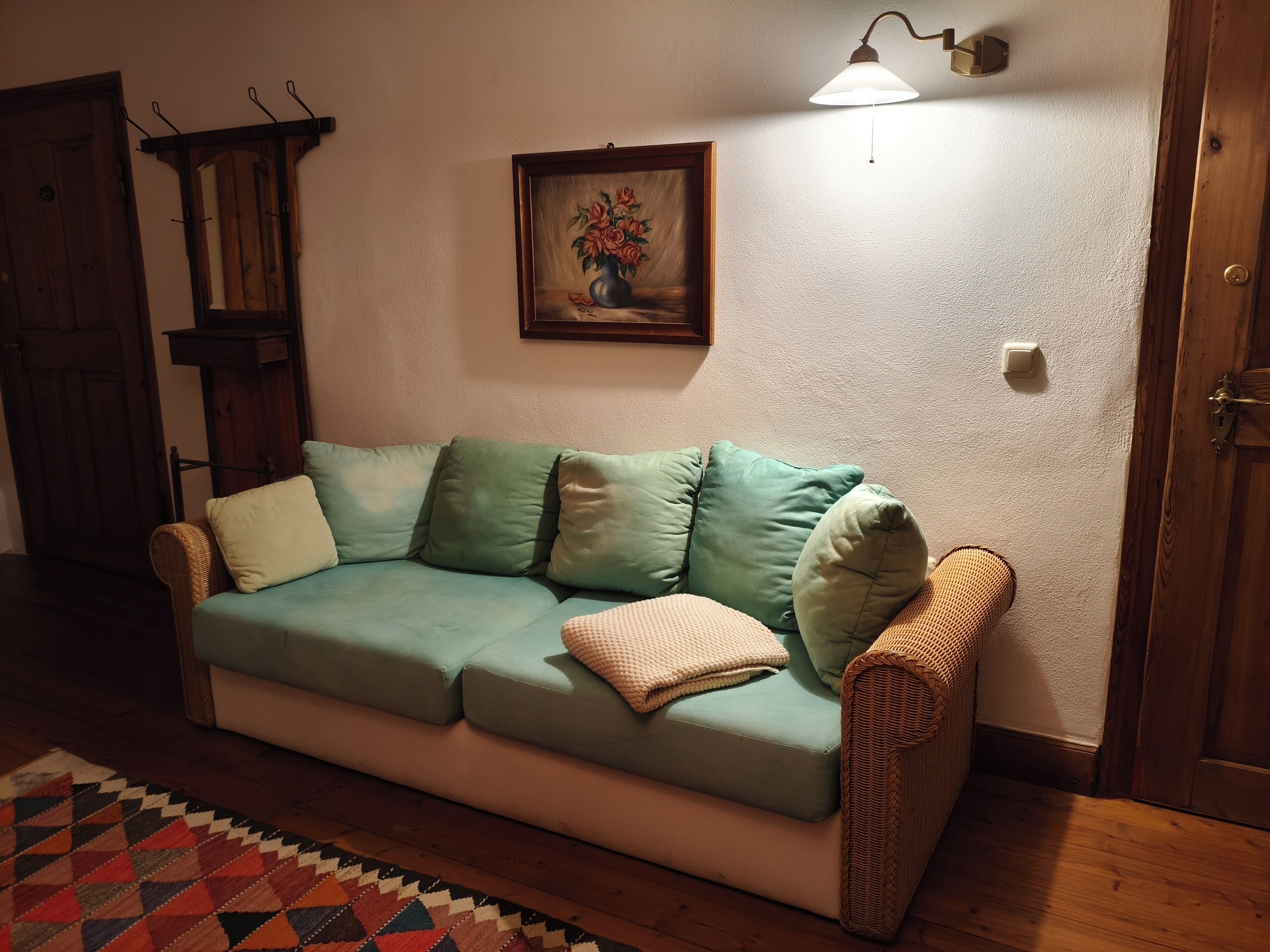 A cozy living room with a teal sofa, a patterned rug, a painting, and a wall-mounted lamp.