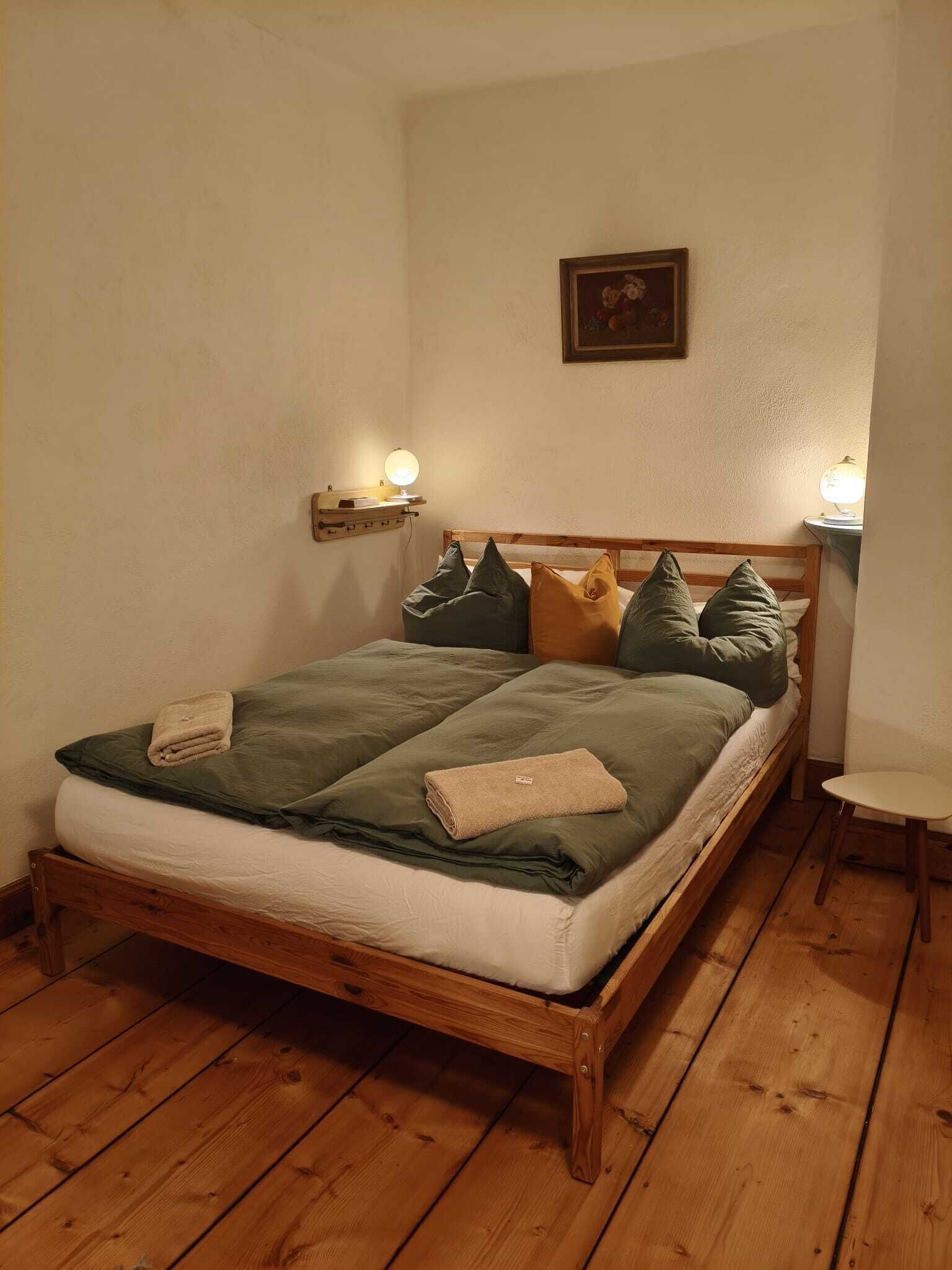 Ein hölzernes Bett mit einer grün-weißen Bettdecke, mehreren Kissen und zwei Nachttischlampen.