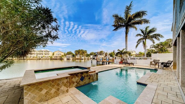 A swimming pool with a tiled deck, surrounded by palm trees and a view of a marina. - Heated Pool, Spa and Fun at Ocean Shore Retreat (Indian Rocks Beach)