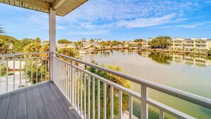 A waterfront view from a covered balcony with a railing, overlooking a calm lake, boats, and a marina with buildings in the background. - Heated Pool, Spa and Fun at Ocean Shore Retreat (Indian Rocks Beach)