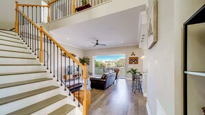 A spacious living area with a staircase, a balcony, and a view of the outdoors. - Heated Pool, Spa and Fun at Ocean Shore Retreat (Indian Rocks Beach)