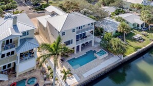 A large, multi-story house with a swimming pool, outdoor seating, and a dock by the water. - Heated Pool, Spa and Fun at Ocean Shore Retreat (Indian Rocks Beach)