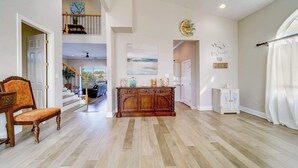 A spacious living area with hardwood flooring, a wooden bench, a console table, and a staircase leading to an upper level. - Heated Pool, Spa and Fun at Ocean Shore Retreat (Indian Rocks Beach)