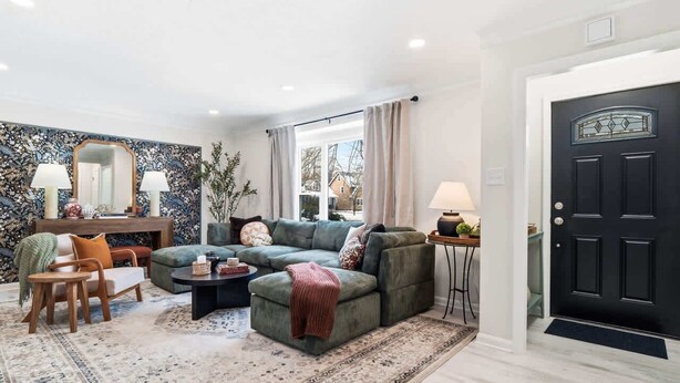 Una sala de estar con un sofá seccional, una mesa de centro y una alfombra. Se ve una puerta con un panel de vidrio decorativo y otra puerta negra.