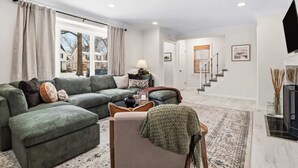 Sala de estar con un sofá modular, una mesita y un sillón. Se ve una escalera que conduce a otra habitación.