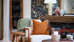 Una sala de estar acogedora con chimenea, un plaid verde de punto, una mesa de centro de madera y un cojín rojo.