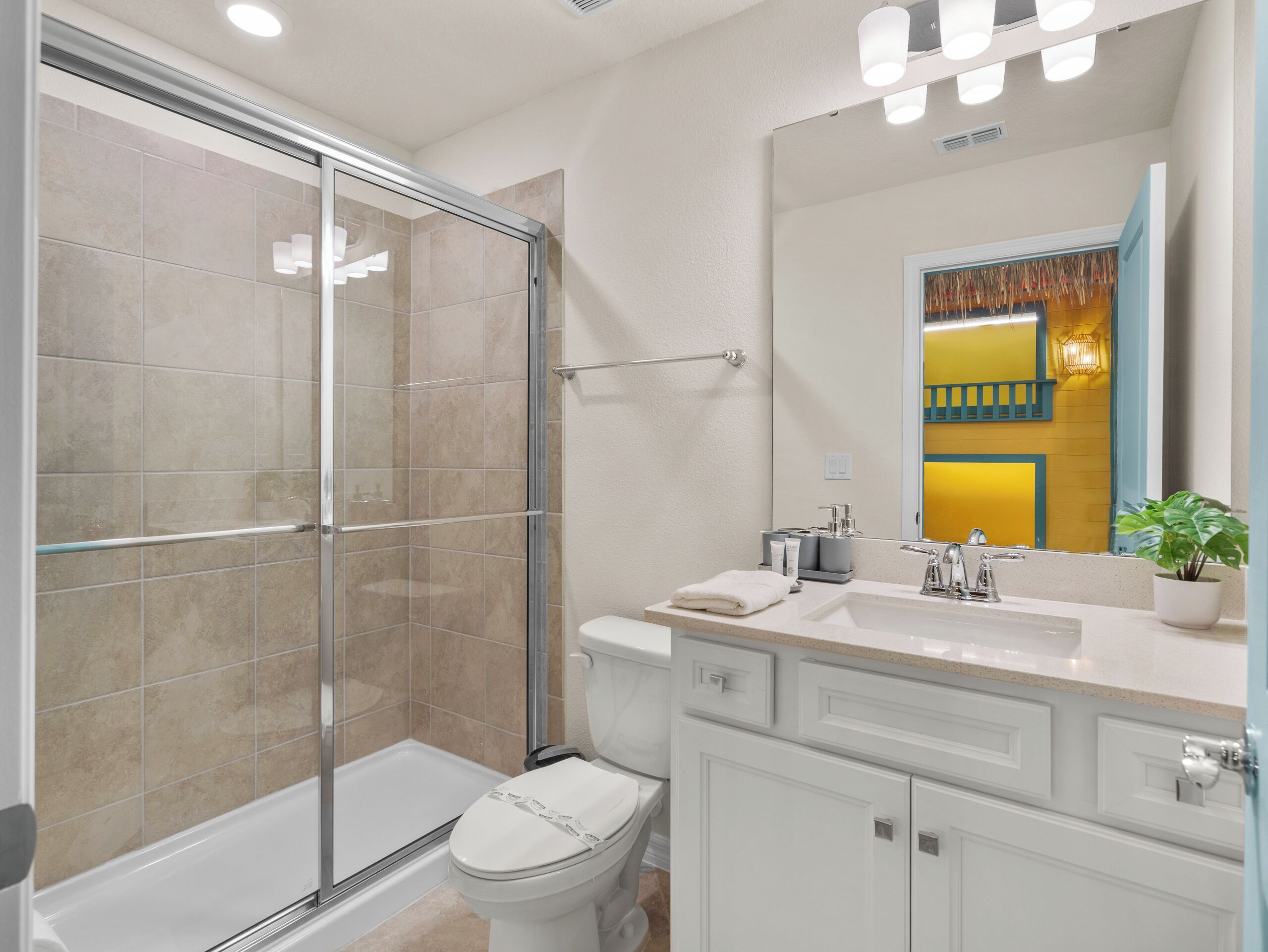 A bathroom with a glass-enclosed shower, a toilet, a sink with a mirror, and a potted plant.
