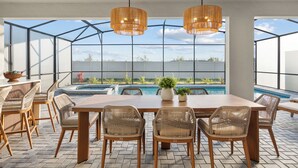 Un espace repas extérieur moderne avec vue sur la piscine, doté de mobilier en osier et d’un éclairage suspendu.
