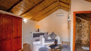 Una habitación con un sofá blanco curvo, cojines grises, una mesita redonda con una lámpara y un armario de madera.