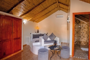 Ein Zimmer mit einem gebogenen weißen Sofa, grauen Kissen, einem kleinen runden Tisch mit einer Lampe und einem Holzschrank.