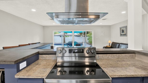 A kitchen with a stainless steel stove, granite countertops, and a view of a backyard with a pool. - Amazing Home with Heated Pool! Sleeps 10! Book Now! Minutes from everything.  (St. Petersburg)